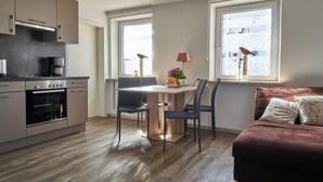 A modern kitchen with a built-in oven and a dining area with a table and chairs. There is a sofa with cushions and a window with a view of the outside. - Ferienwohnung Rebe (Günzburg)