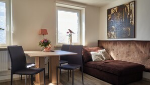A modern living room with a wooden dining table, two chairs, a brown sofa, and a large abstract art piece on the wall. - Ferienwohnung Rebe (Günzburg)