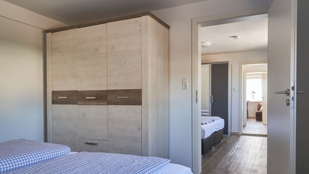 A hotel room with two beds, a wardrobe, and a view into another room. - Ferienwohnung Rebe (Günzburg)