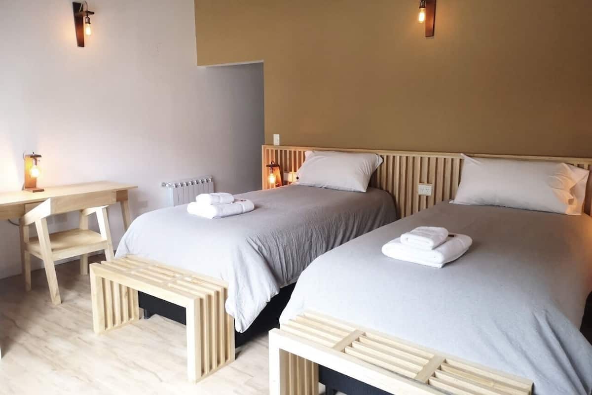 Una habitación de hotel con dos camas, un escritorio de madera y luces fijadas a la pared.