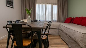 A dining area with a wooden table and chairs, a vase with a plant, and a sofa with red cushions.
