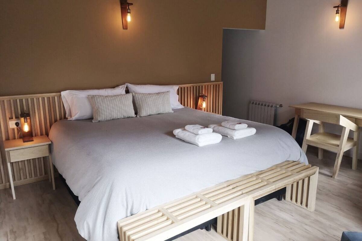 Un dormitorio ordenado con cama, mesitas de noche, un escritorio y un banco.