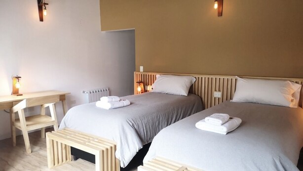 A hotel room with two beds, a wooden desk, and wall-mounted lights.