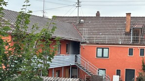 Un edificio de dos pisos con fachada roja, escalera gris y tejado de tejas.