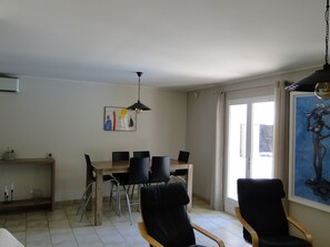 A dining area with a wooden table and black chairs, a hanging light fixture, and a painting on the wall.