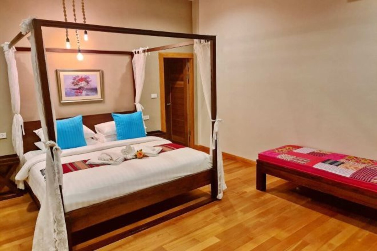 Una cama con dosel y cuatro columnas, una mesita de noche pequeña y una colcha roja.