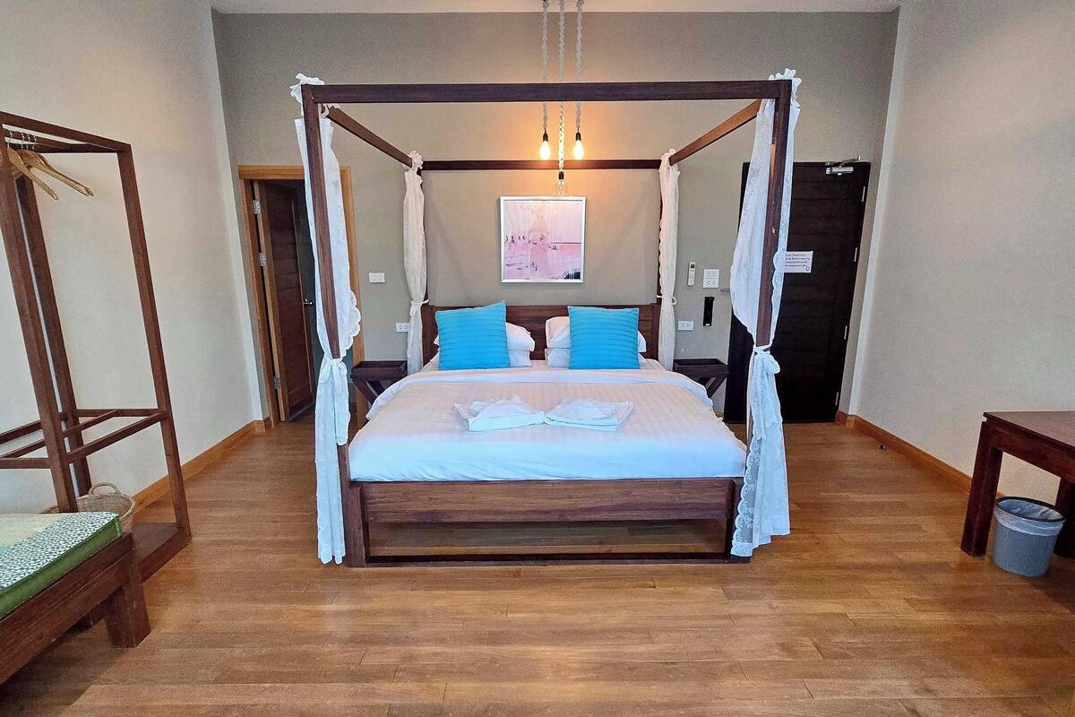 Una cama con dosel con cortinas blancas, suelo de madera y un cuadro en la pared.