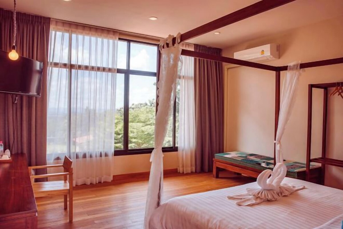 Une chambre à coucher avec un lit à baldaquin, une télévision et une vue sur la verdure environnante.