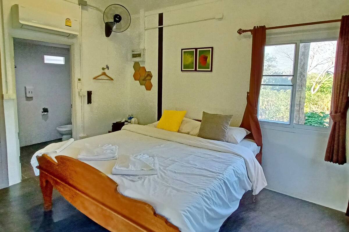 Un dormitorio con una cama, una mesita de noche, una lámpara colgante, una ventana con cortinas y una puerta.