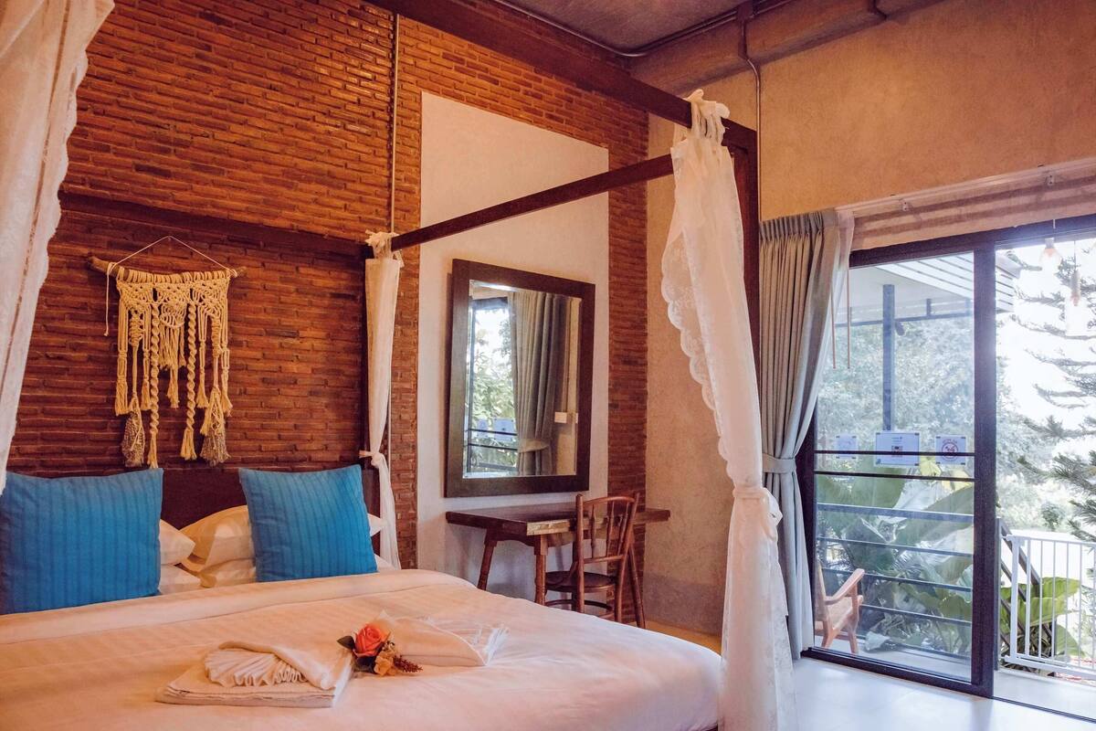 Un dormitorio con una cama con dosel, un colgador de macramé, un espejo y vistas al exterior.