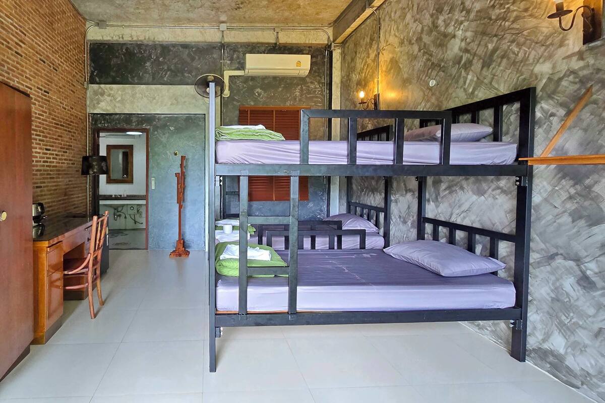 Habitación con literas, un escritorio, una silla, una mesita y una pared de ladrillo.