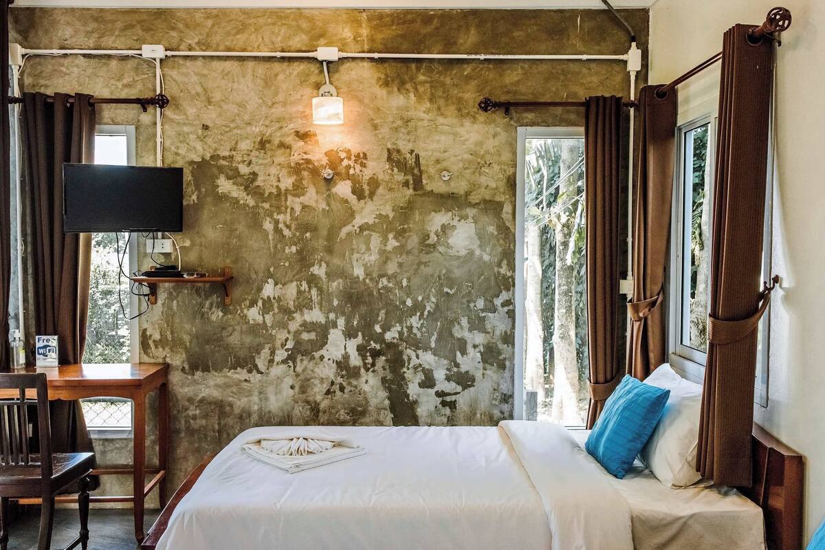Un dormitorio con cama, escritorio, televisor y ventana con cortinas.