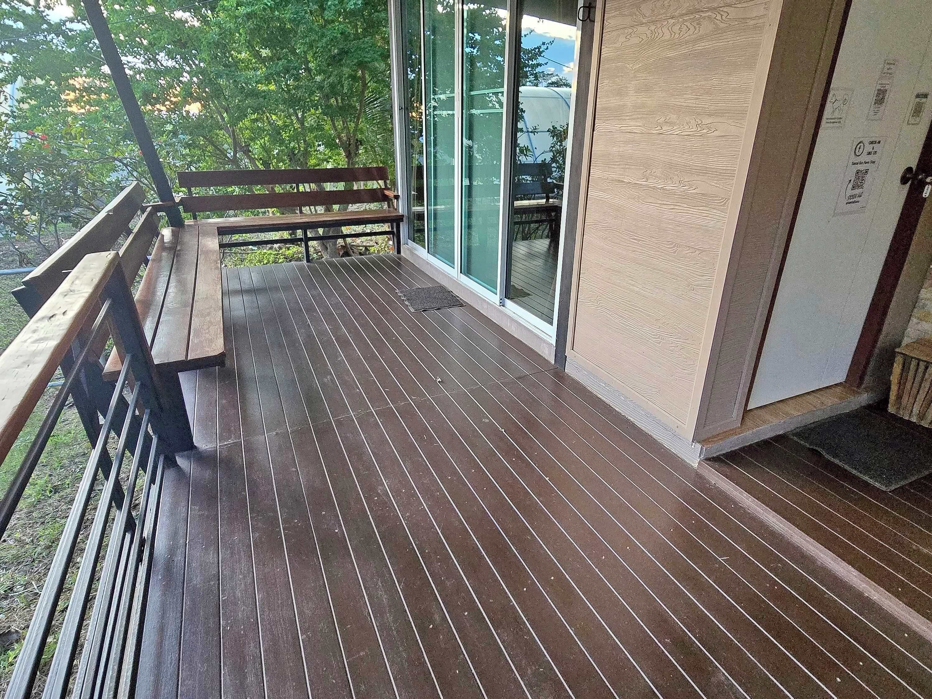 A wooden deck with a bench, glass doors, and a view of greenery.