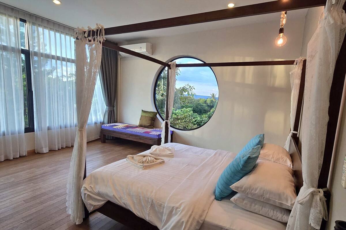 Una cama con dosel, un ventanal redondo y vistas al verdor exterior.