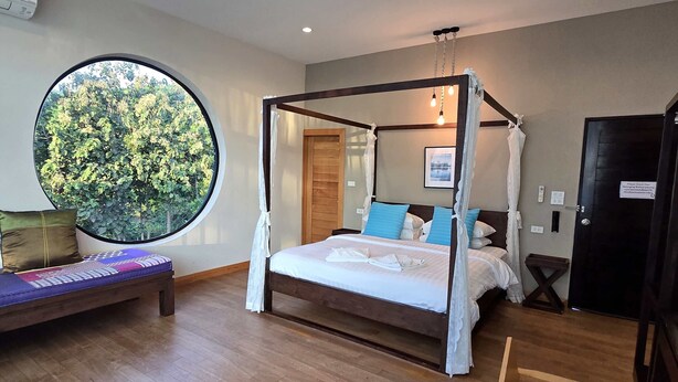 Una cama con dosel y cuatro columnas, con vista a la vegetación a través de un gran ventanal circular.