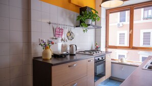 Cuina amb rajoles blanques, forns, vitroceràmica i finestra amb vista a edificis.