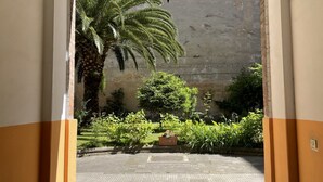 Un pati exterior amb una palmera, un fanal penjant i una jardiniera amb flors.