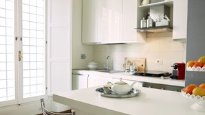 A modern kitchen with white cabinets, a stainless steel countertop, a kettle, and a fruit bowl.