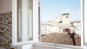 A window with a view of a cityscape, including buildings with tiled roofs and a clear sky.
