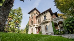 A large, historic building with a prominent tower, surrounded by lush greenery and trees.