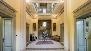 A grand hallway with a staircase, ornate ceiling, and classical decor.