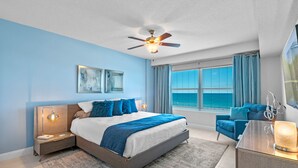 Une chambre à coucher comprenant un lit, des tables de chevet, un bureau, une chaise, un ventilateur de plafond et une fenêtre avec des rideaux.