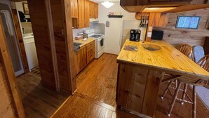 Een keuken met houten kastjes, een fornuis, een koelkast en een eethoek met een houten tafel en stoelen.