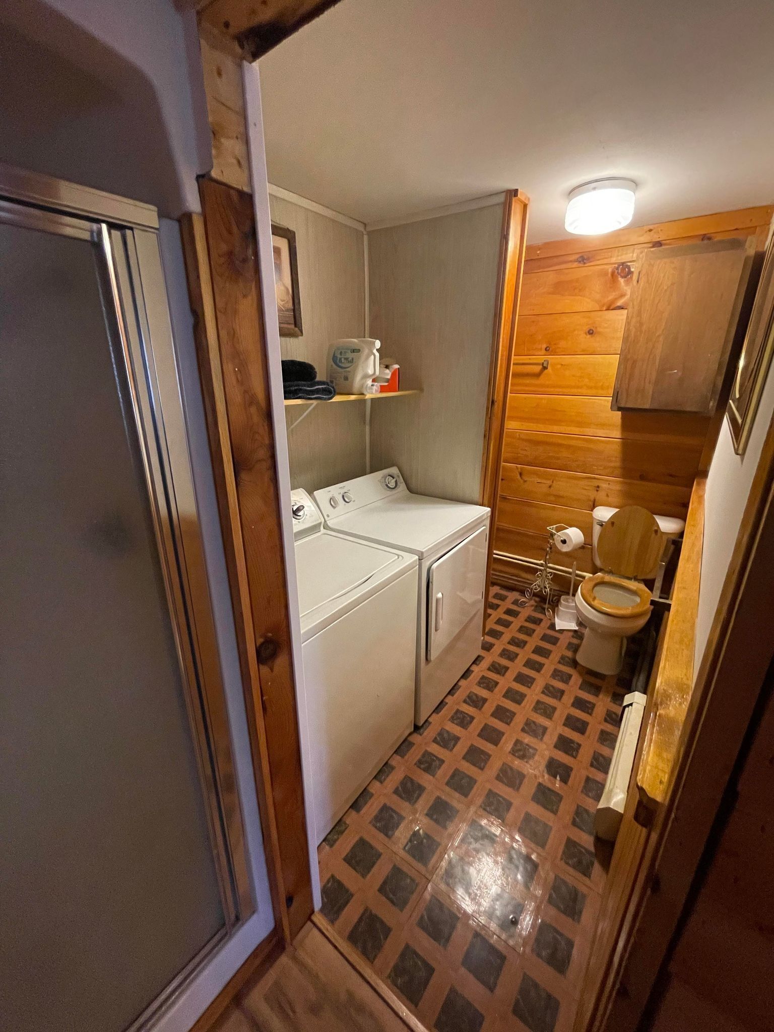 A compact bathroom with a washing machine, toilet, and a shelf with toiletries.