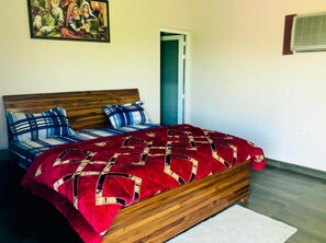 A bedroom with a wooden bed frame, a red and black patterned bedspread, and blue striped pillows. - Gurugram Aravali Farmhouse  (Sohna)