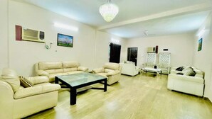 A living room with beige leather sofas, a glass coffee table, and a chandelier. - Gurugram Aravali Farmhouse  (Sohna)