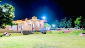 A modern building with a flat roof, a staircase leading to the entrance, and a well-maintained lawn. - Gurugram Aravali Farmhouse  (Sohna)