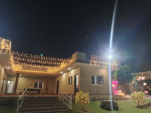 A modern building with a covered outdoor area, steps leading up to the entrance, and string lights. - Gurugram Aravali Farmhouse  (Sohna)