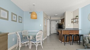 Ein Essbereich mit Tisch und Stühlen, eine Küche mit Barhocker und ein Deckenventilator.