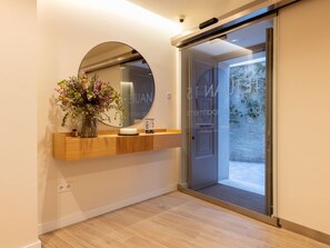 Un interior moderno con una consola de madera, un espejo redondo y un jarrón con flores.