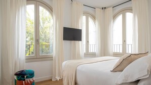 A bedroom with a bed, a TV mounted on the wall, and large windows with curtains. - Hommyhome Tetuán 15 Boutique - 202 (Sevilla)