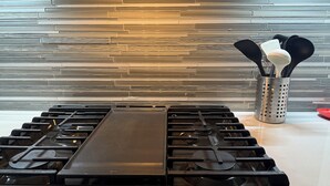A kitchen with a modern gas stove, stainless steel countertops, and a textured backsplash. - Home away from home!!! (Sun Prairie)