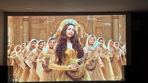 A large screen displaying a scene with a central figure in traditional attire, surrounded by others in similar costumes, suggesting a cultural or historical performance. - Home away from home!!! (Sun Prairie)