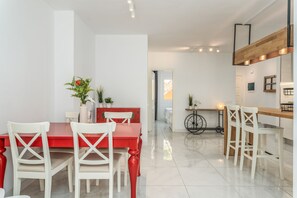 Uma sala de jantar moderna com mesa vermelha e cadeiras brancas, área de cozinha com detalhes em madeira e interior limpo e claro.