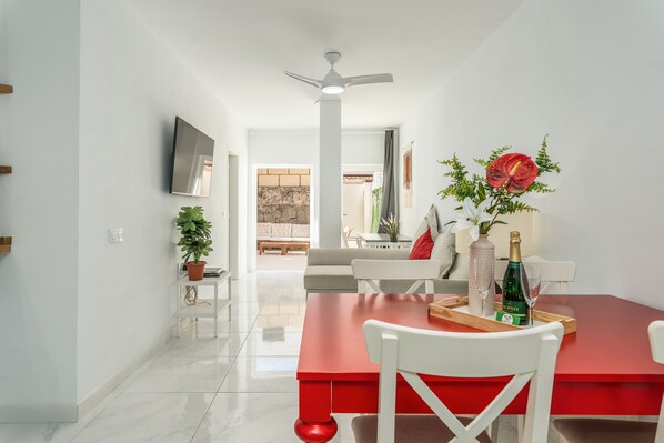 Uma zona de refeições moderna com mesa vermelha, cadeiras brancas, ventoinha no teto e planta em vaso.
