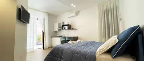 A modern hotel room with a bed, a TV, a kitchenette, and a bathroom.