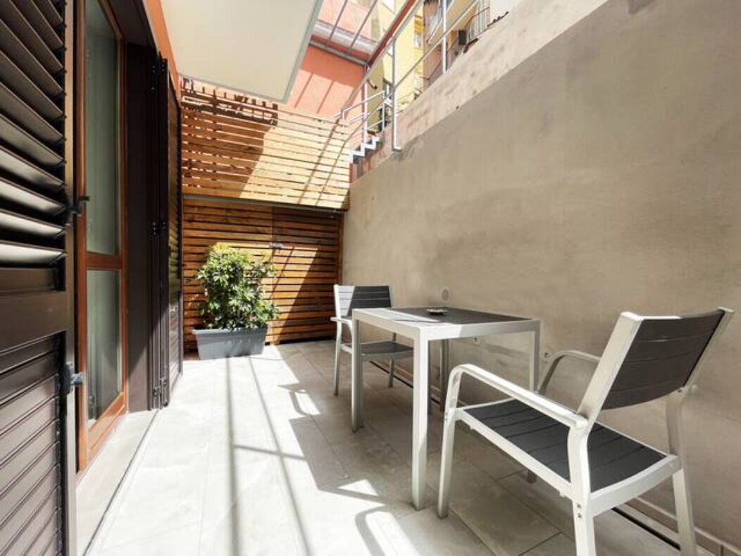 Un pequeño patio al aire libre con una mesa, dos sillas, una planta en maceta y un muro de listones de madera.