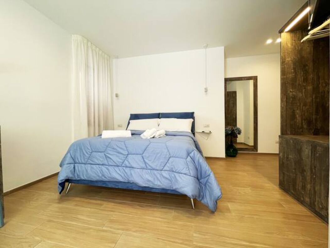 A bedroom with a bed, wooden flooring, a white curtain, and a wooden wall.