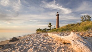 Een zandstrand met een vuurtoren en een groot blok hout op de voorgrond.