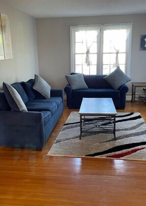 Un salón con dos sofás azul oscuro, una mesa de centro blanca y una alfombra estampada.