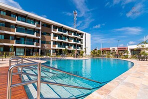 A modern hotel with a large swimming pool, multiple balconies, and a clear blue sky. - Mana Beach Experience B221- Carpediem (Ipojuca)