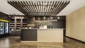 A modern hotel reception area with a wooden slatted ceiling, a reception desk, and a minibar. - Home2 Suites By Hilton Cookeville (Cookeville)