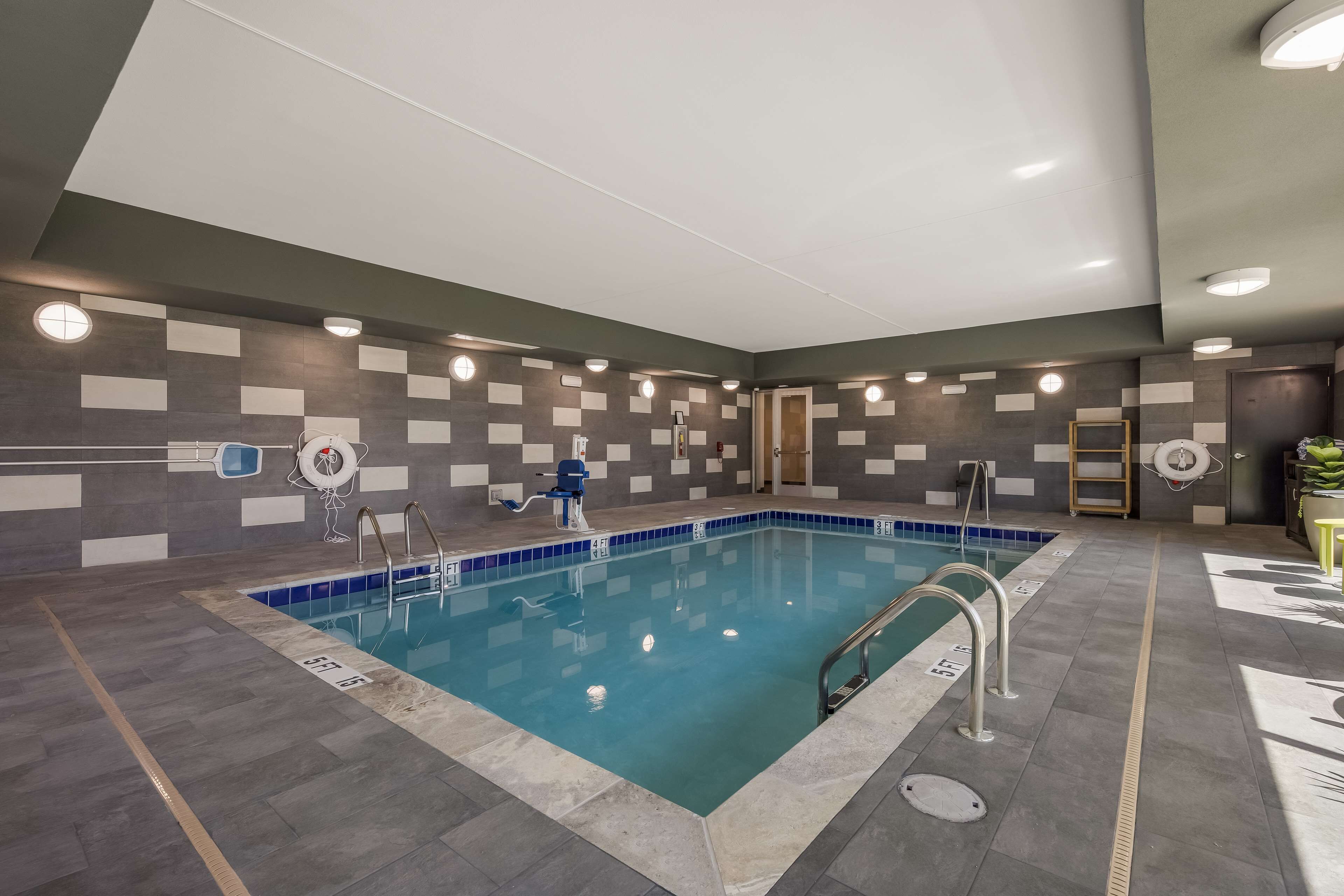 En inomhuspool med kakelbeklädda väggar, en blå poolkant och flera poolstegar.