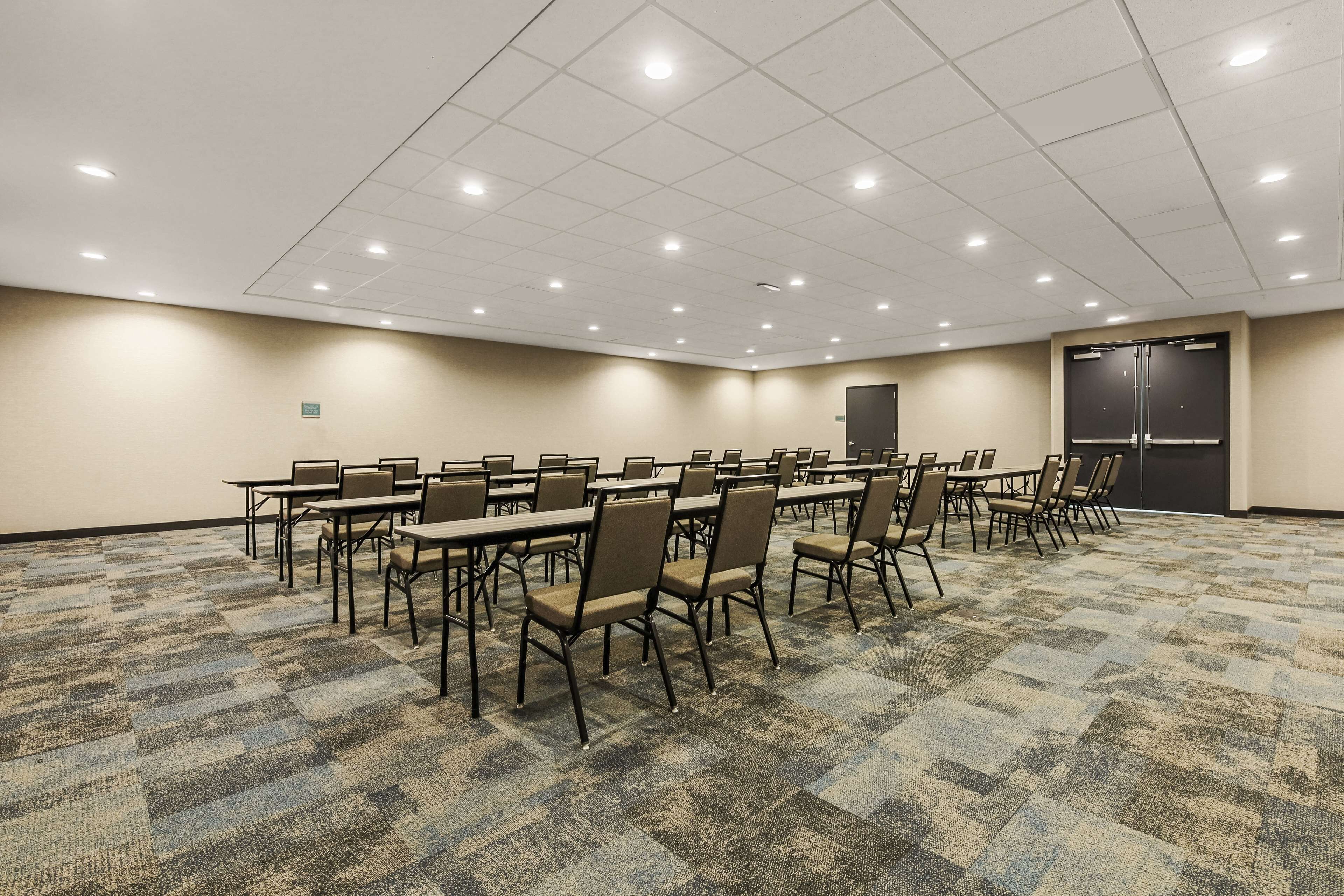 Une salle de conférence avec plusieurs tables et chaises, un sol recouvert de moquette et une porte au fond.