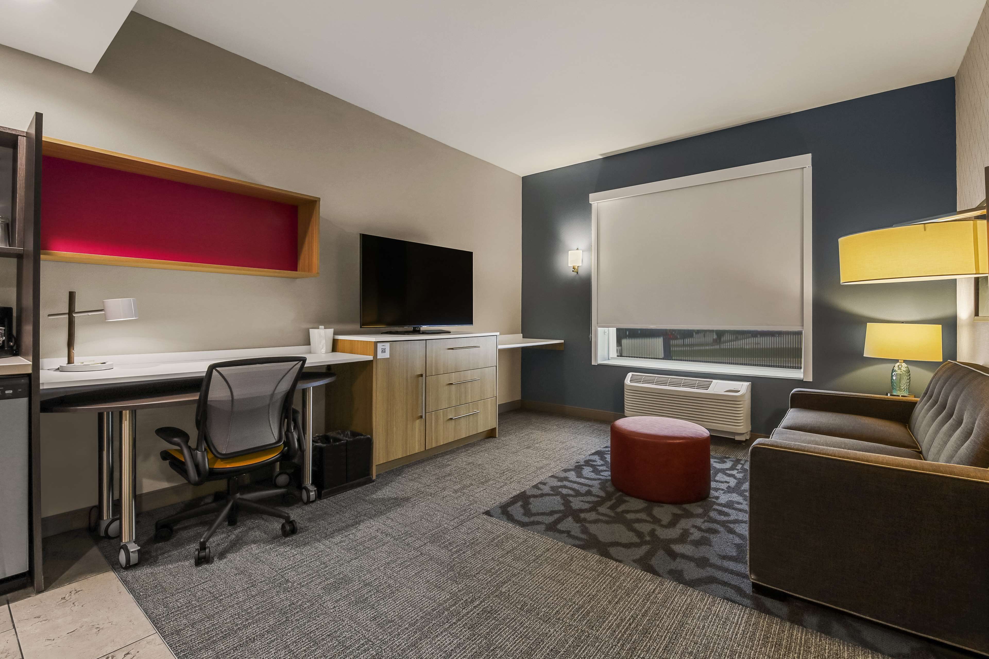 Une chambre d’hôtel compacte comprenant un coin cuisine, un bureau avec une chaise, un téléviseur à écran plat, un canapé et une fenêtre donnant sur un paysage agréable.