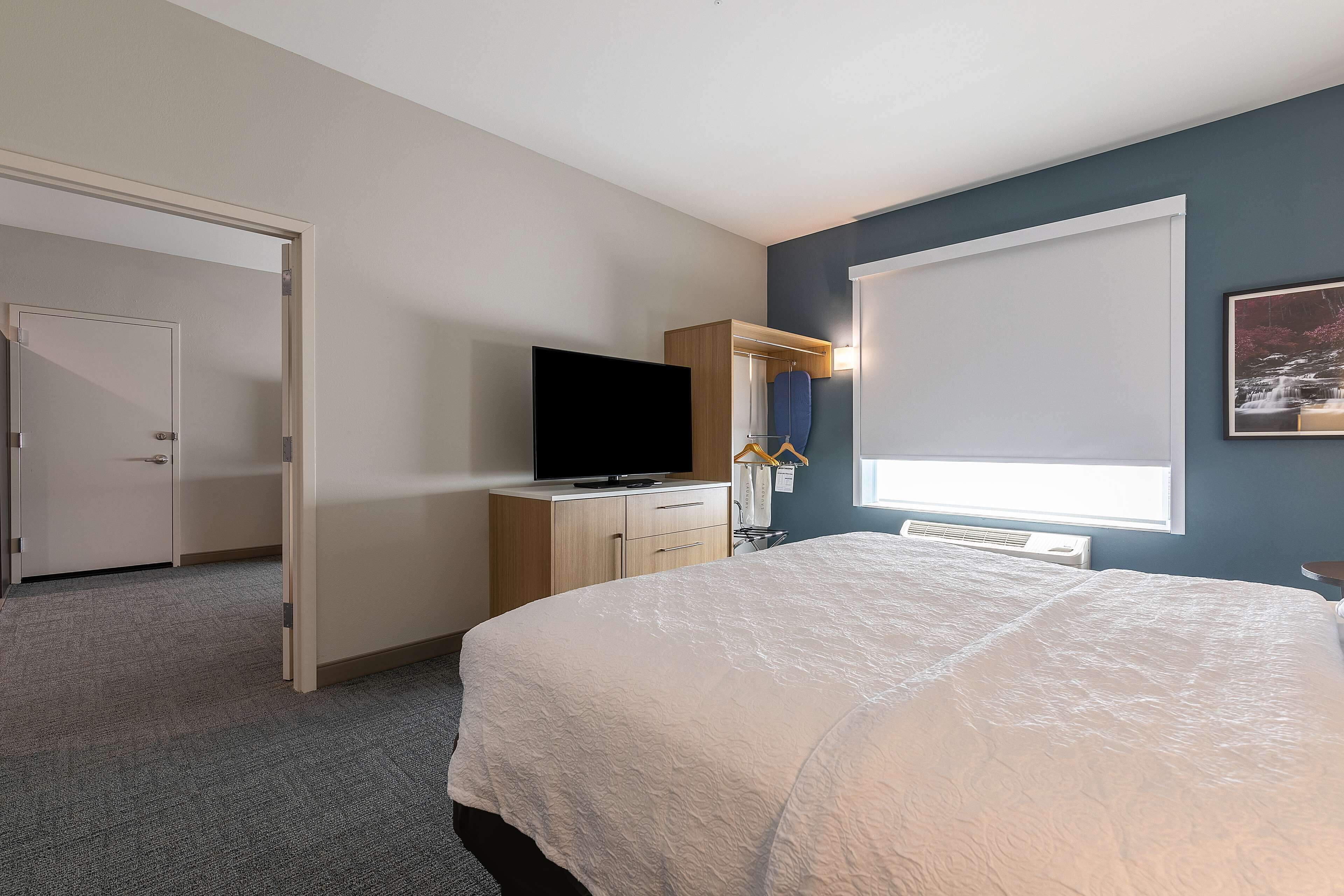 A bedroom with a bed, a television, a wardrobe, and a window with blinds.